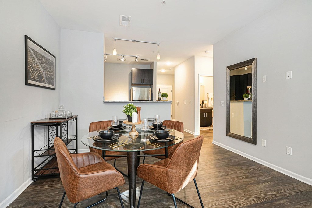 A dining room with a glass table and brown chairs.