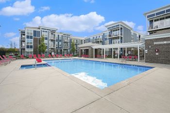 A large swimming pool in front of a building with red lounge chairs.