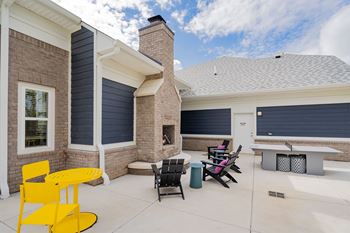 A yellow chair sits in a patio with a brick house in the background.