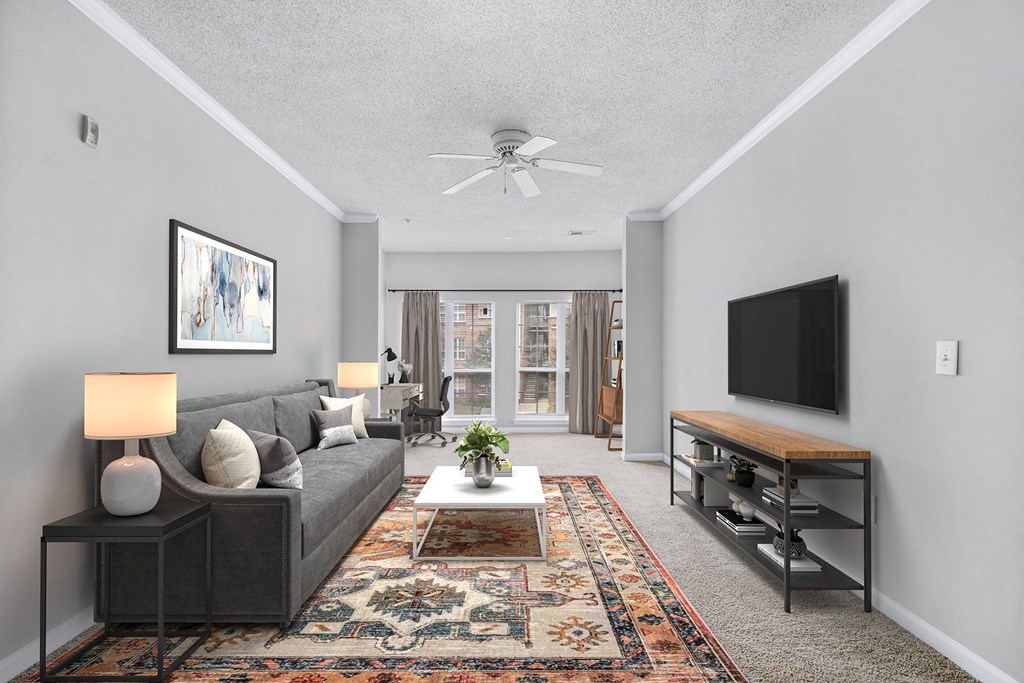 A living room with a grey couch, a rug, a ceiling fan, and a flat screen TV.