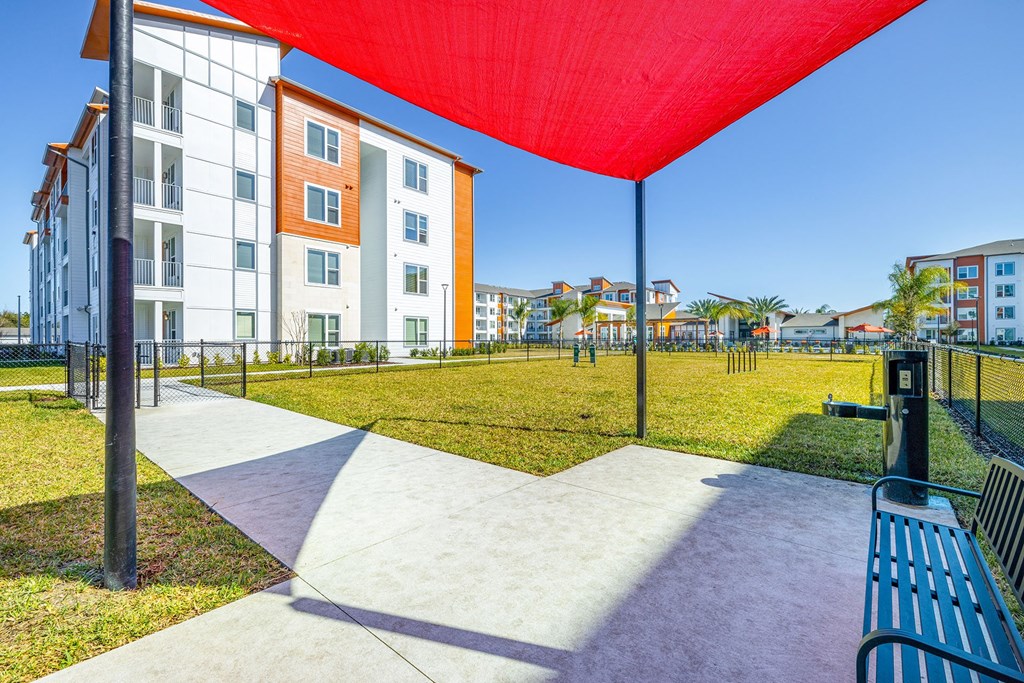 Two-Bedroom Apartments in Daytona Beach, FL - Madison Pointe - Leash-Free Dog Park with Lush Grass, Agility Course, and Bench Under Canopy.