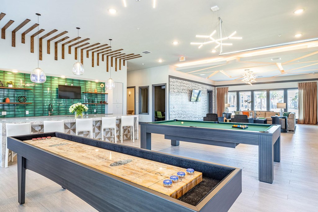 One Bedroom Apartments in Daytona Beach, FL - Madison Pointe - Gaming Room with Billiards and Shuffleboard Tables, Pendant Lighting, Bar with Bar-Style Chairs, TV, and Lounge Seating