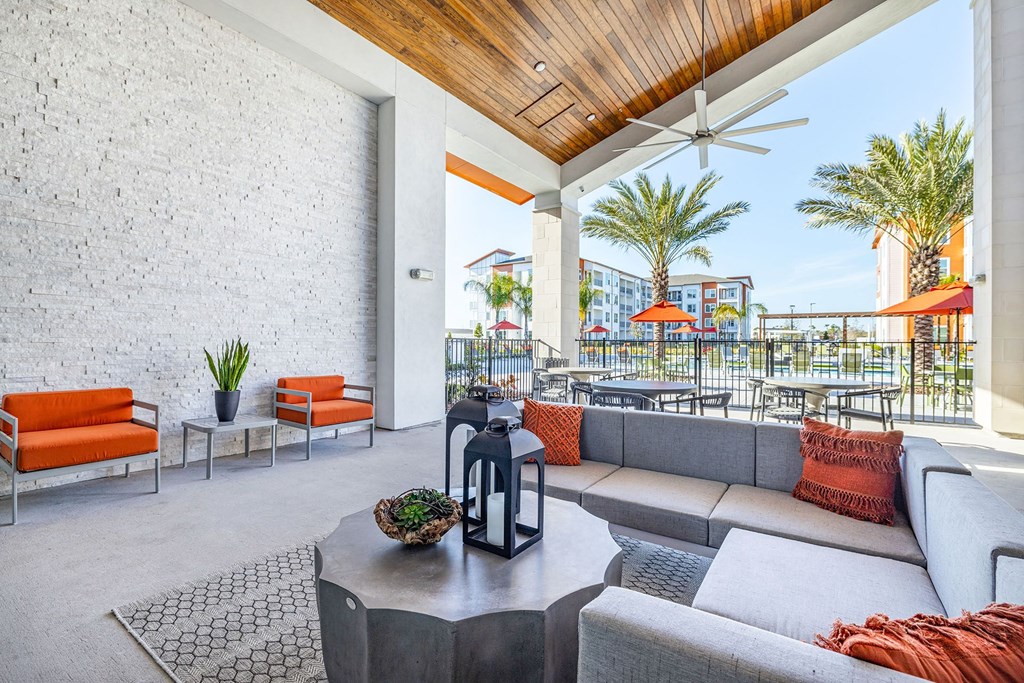 2-Bedroom Apartments in Daytona Beach, FL - Madison Pointe - Clubhouse Patio with a Sectional Sofa, Coffee Table, Armchairs, Outdoor Tables and Chairs, Ceiling Fan, and View of Pool.