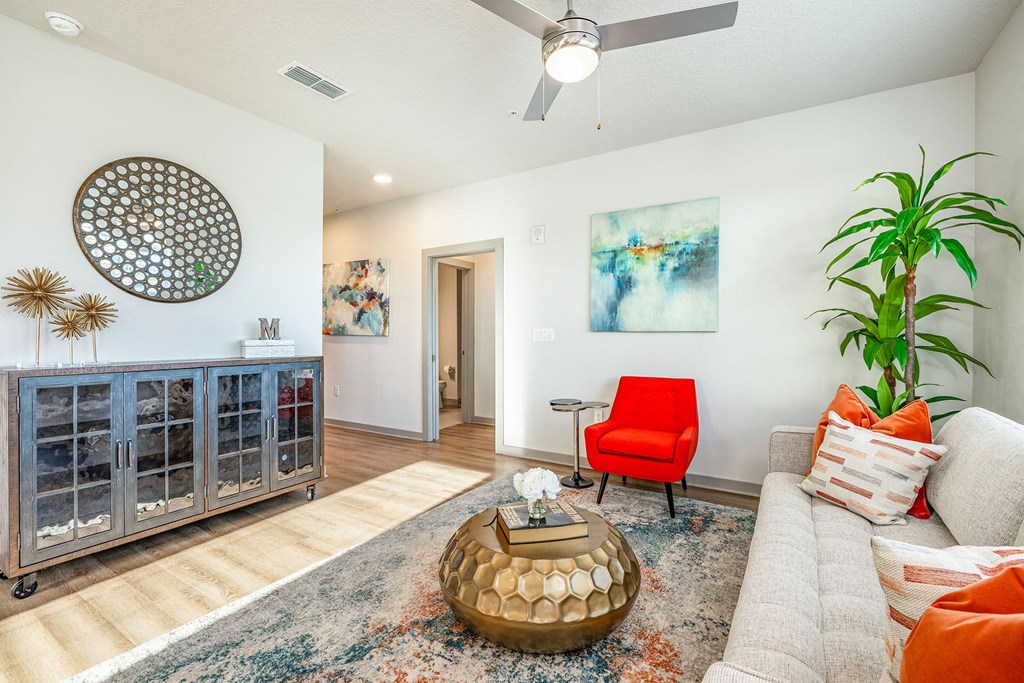 1 Bedroom Apartments in Daytona Beach, FL - Madison Pointe - Living Room with Wood-Style Plank Flooring, Area Rug, Couch, Chair, Round Coffee Table, Cabinet, Wall Art, House Plant, and Ceiling Fan