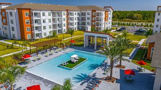 3-BR Apartments In Daytona Beach, FL - Madison Pointe - Birds Eye View Of Pool With Center Island, Tables, Chairs, Umbrella, Lounge Beds, And Palm Trees.