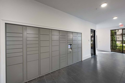 A row of grey lockers in a room with a black door on the right.