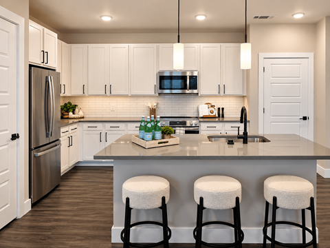 A kitchen with white cabinets and a large island with three stools.