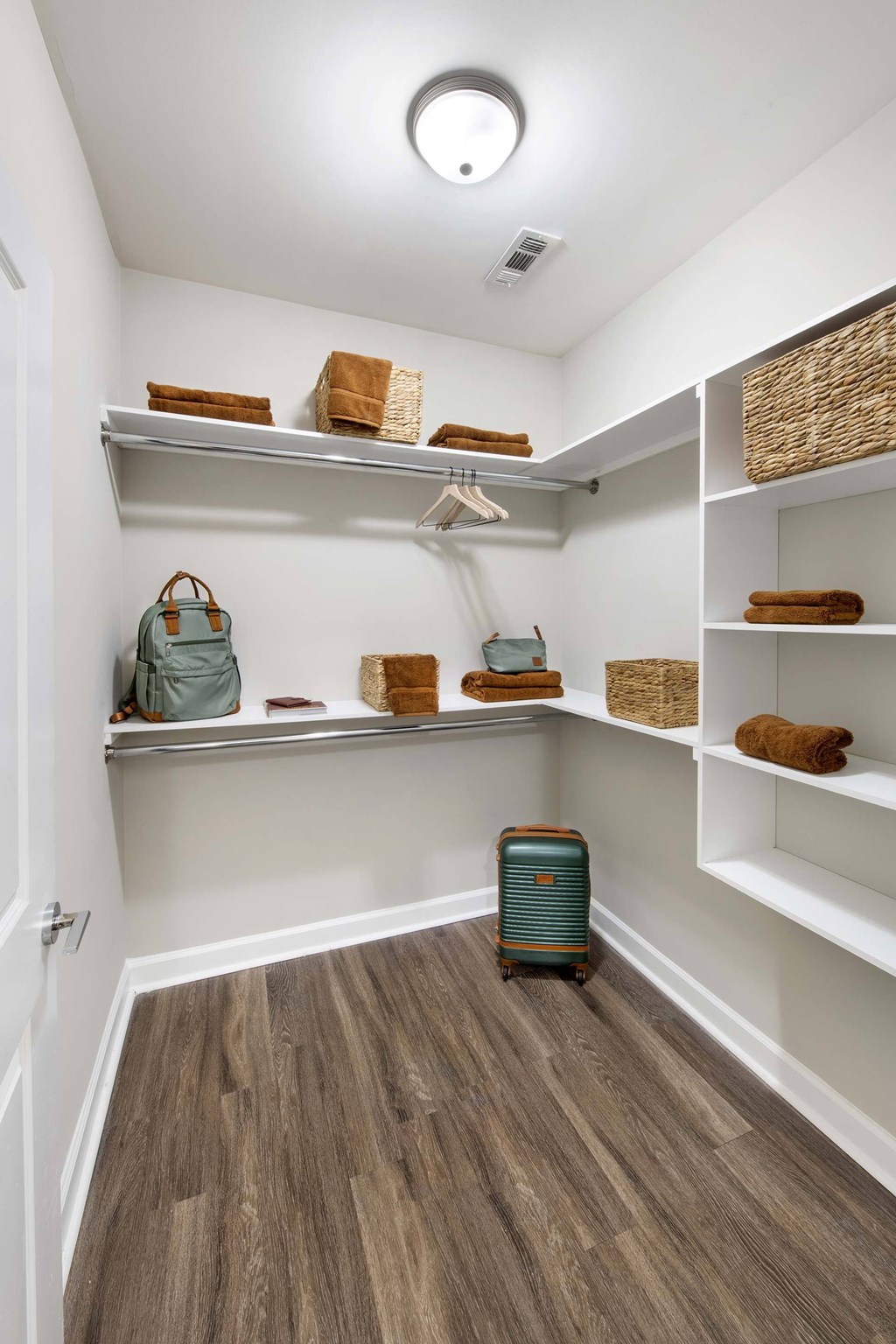 A small closet with a suitcase and a backpack on the shelf.