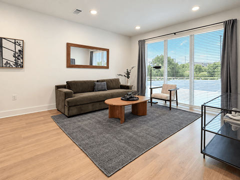 A living room with a grey rug, a brown coffee table, a brown couch, and a mirror on the wall.