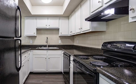 A black refrigerator is in a kitchen with white cabinets.