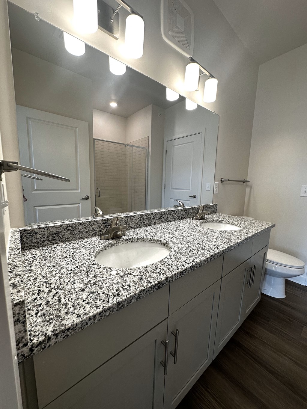 a bathroom with a granite counter top with two sinks and a toilet