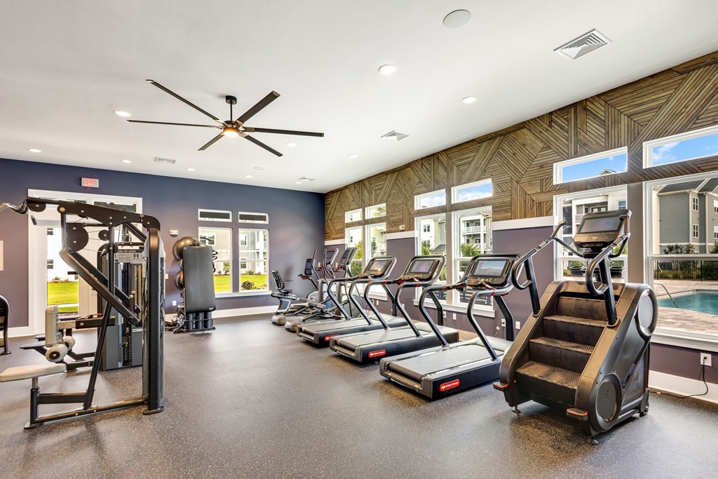 A spacious gym with treadmills, elliptical machines, and a ceiling fan.