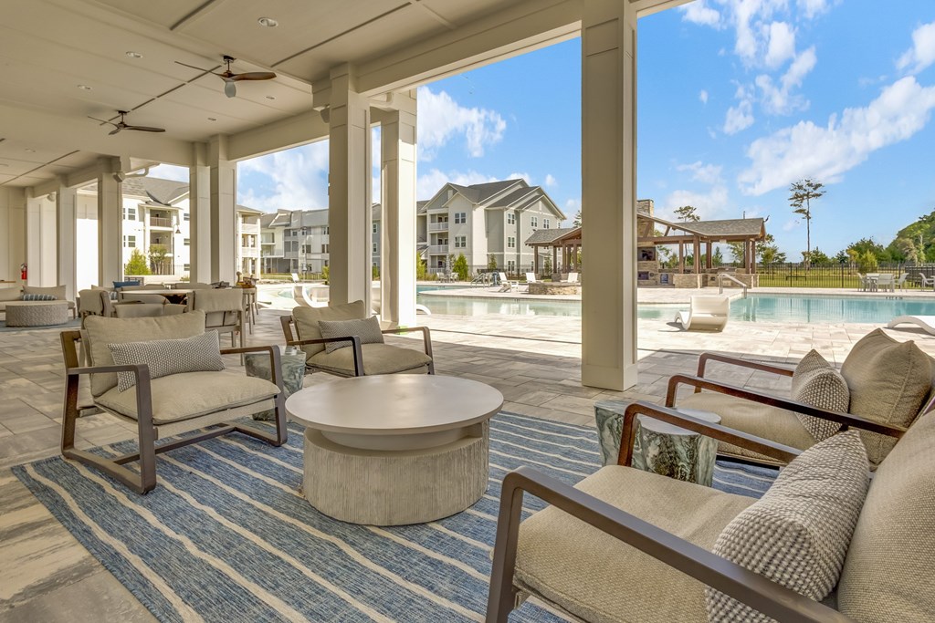 A large, open-air living room with a view of a pool and other buildings.