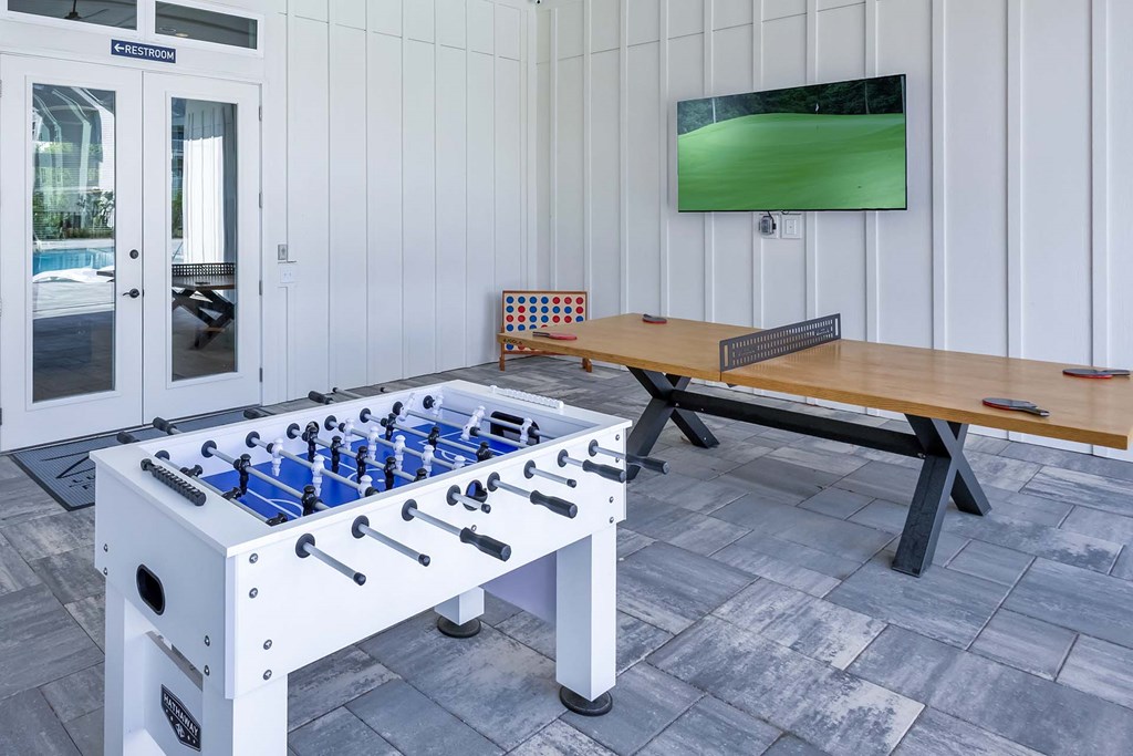 A foosball table is in the middle of a room with a bench and a television.