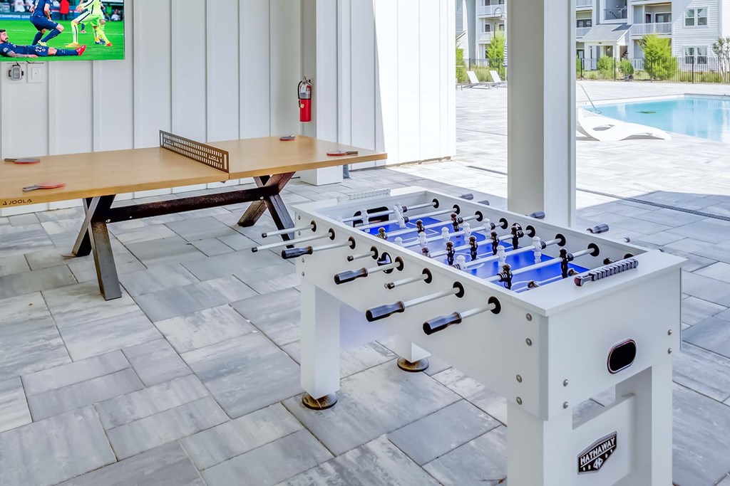 A foosball table is in the middle of a room with a pool table and a bench.