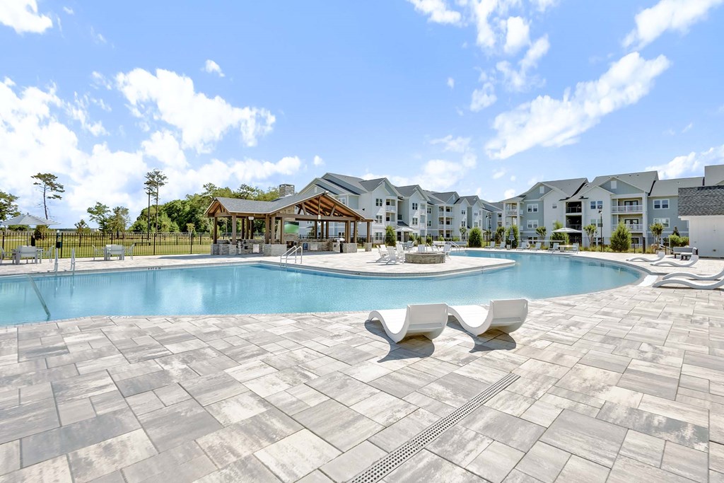 A large swimming pool surrounded by white lounge chairs and a building in the background.