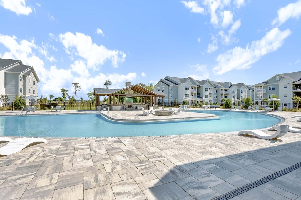 A large swimming pool surrounded by a stone patio and a row of houses in the background.