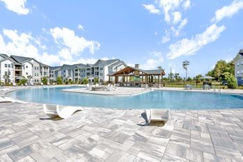A large swimming pool surrounded by a stone patio and lounge chairs.