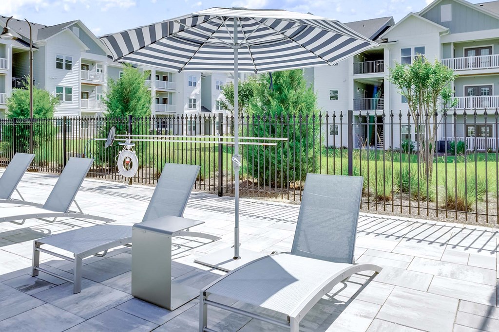 A patio with chairs and a table with a striped umbrella over it.
