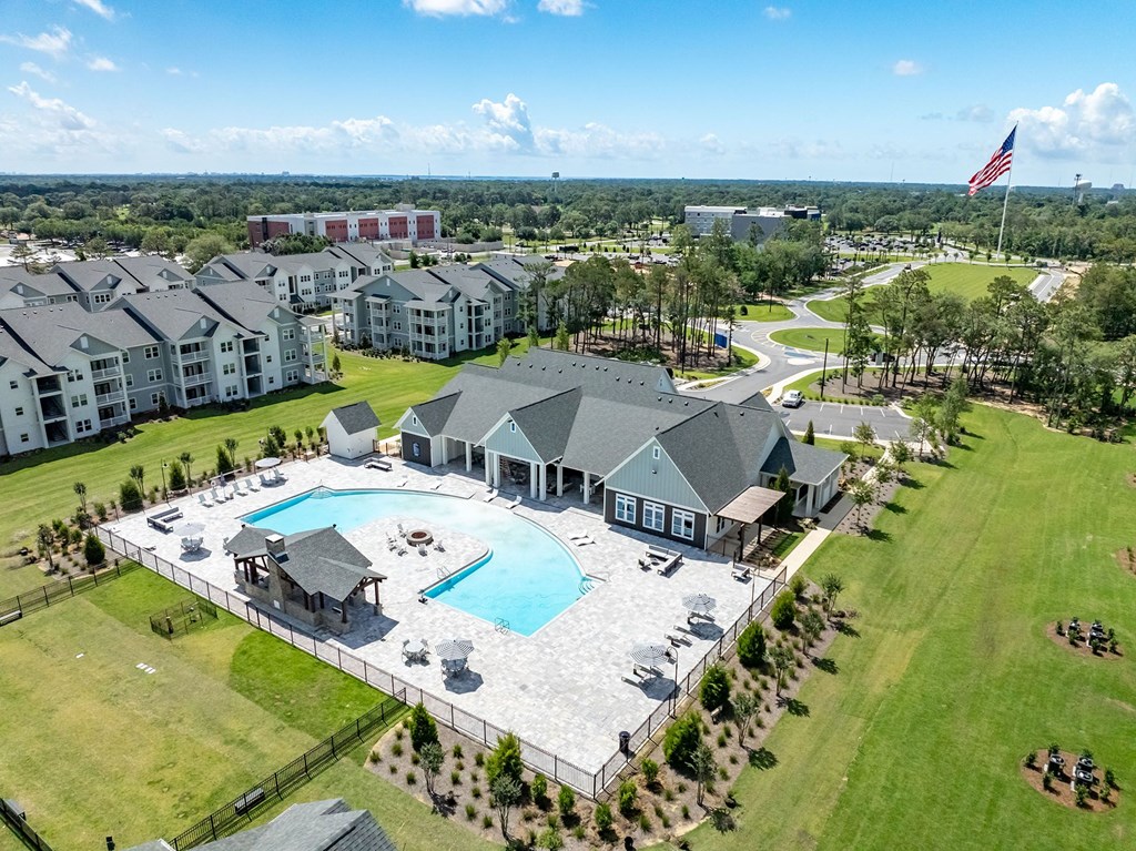 A large swimming pool is surrounded by a grassy area and a few buildings.