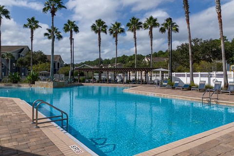A swimming pool surrounded by palm trees and lounge chairs.