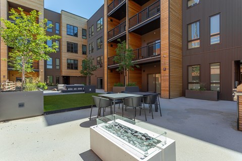 A modern outdoor dining area with a table and chairs surrounded by apartment buildings.
