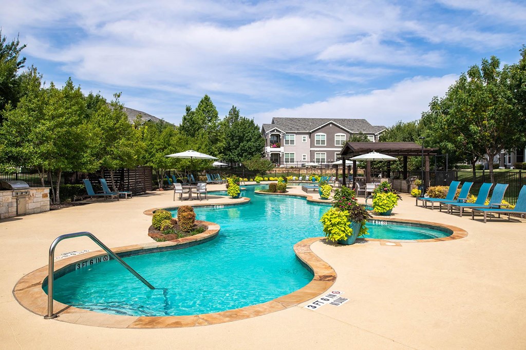 a swimming pool with lounge chairs and umbrellas with a house in the background a swimming pool with lounge chairs and umbrellas with a house in the background at Orion McCord Park, Little Elm, TX, 75068