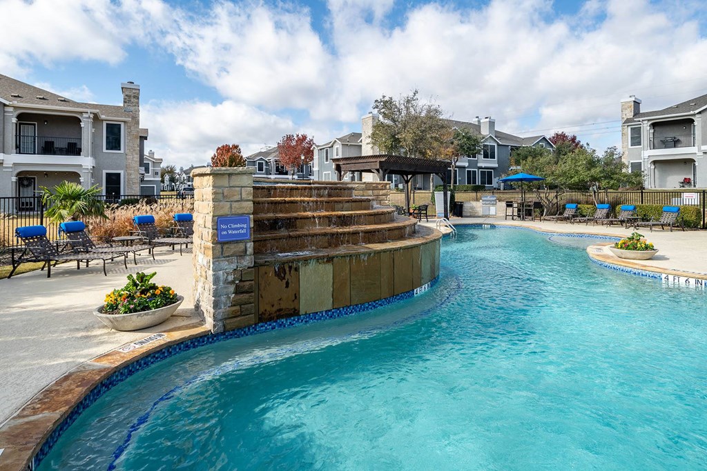 a resort style swimming pool with a stone waterfall  at Orion Prosper Lakes, Prosper