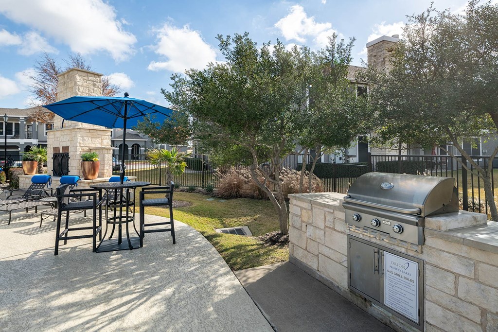 a patio with a grill and a table with chairs and an umbrella  at Orion Prosper Lakes, Prosper
