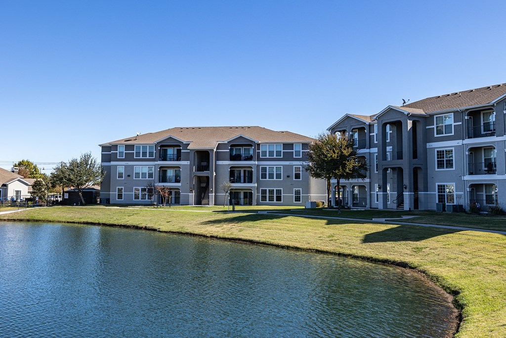 an apartment building overlooks a pond in front of a grass field  at Orion Prosper, Prosper, TX
