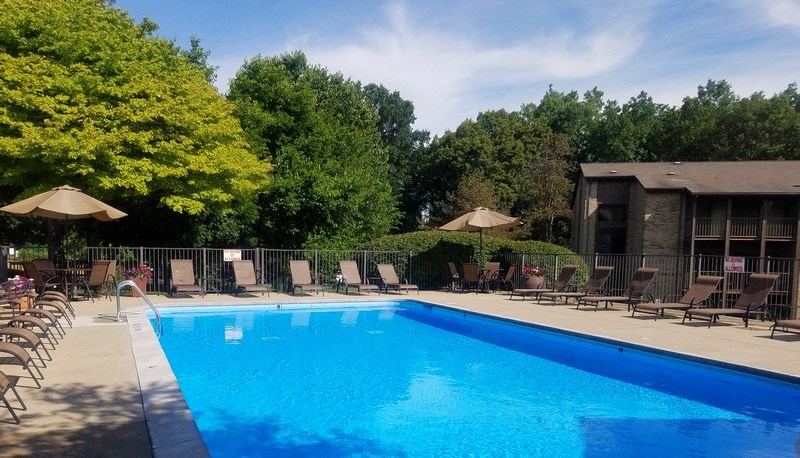 a swimming pool with chaise lounge chairs and umbrellas in front of a building at Winchell Way Apartment , Kalamazoo, MI