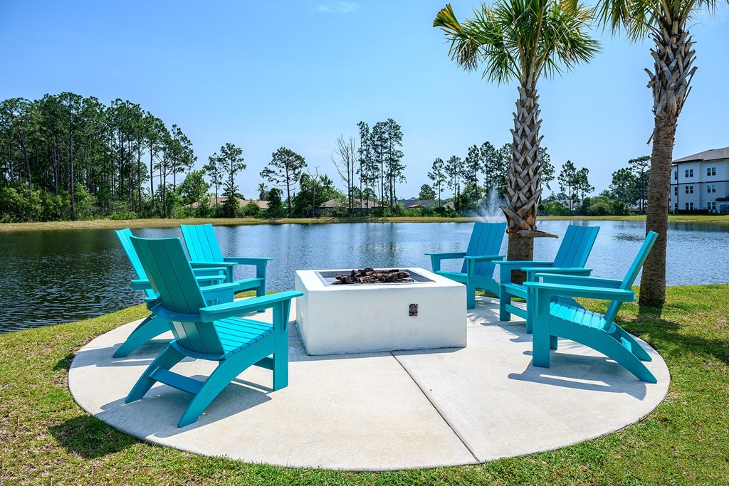 two blue chairs sitting around a fire pit next to a lake