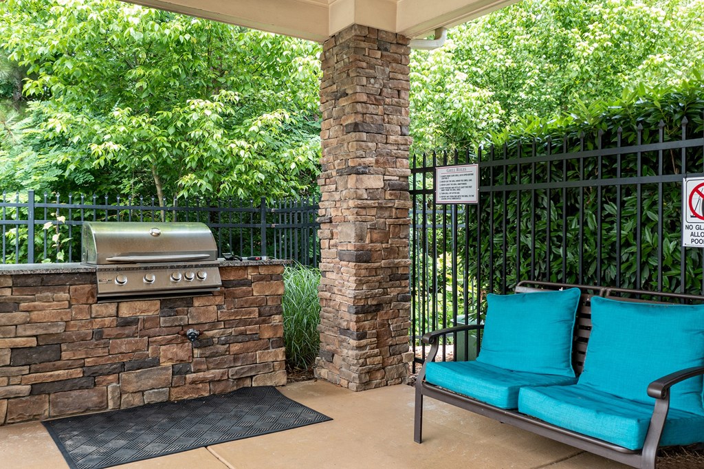 a patio with blue chairs and a grill and a bench