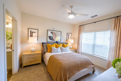 1-Bedroom Luxury Apartments in Athens, GA - Classic City Flats - Bedroom with Carpeted Flooring, Large Bed, Nightstands with Lamps, Ceiling Fan, Large Window, and Attached Bathroom.
