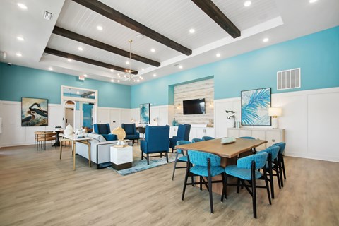 Luxury Apartments for Rent in Flagler Beach, FL - Preserve at Flagler Beach - Resident Lounge With Blue Accent Walls, Dining Table, Sofa Seating, High Ceilings, Wood Beams, And Wood Style Flooring.