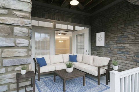 A patio with a white couch, a coffee table, and a stone wall.