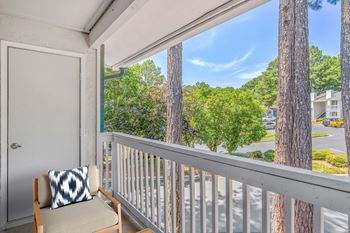 A balcony with a chair and a pillow with a view of trees and a building.