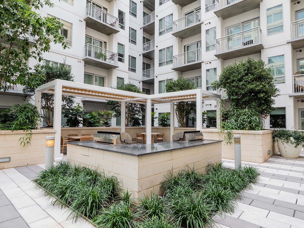 Luxury Apartments Near Georgia Tech, Midtown Atlanta, GA - Trace Midtown - Grilling Station With Granite Countertop, Built-in Stainless Steel Grills, and Tables with Chairs Under White Pergola.