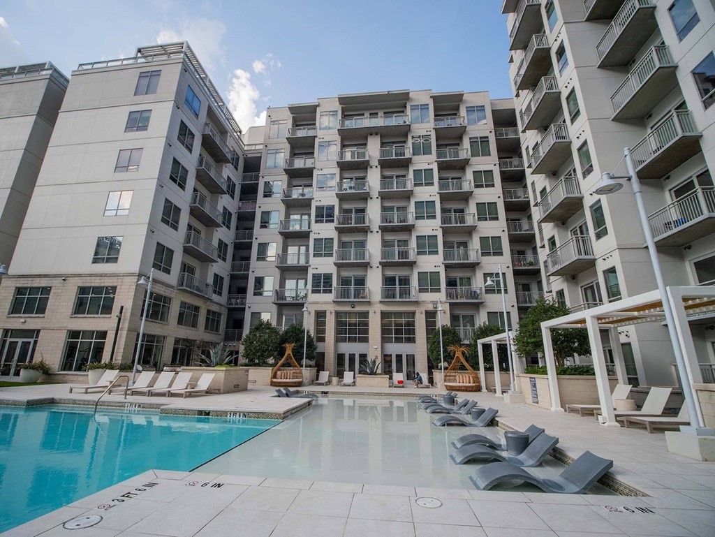 Luxury Apartments Near Piedmont Park, Midtown Atlanta, GA - Trace Midtown - Swimming Pool With Poolside and Submerged Loungers, Cabanas, and View of Apartment Complex.