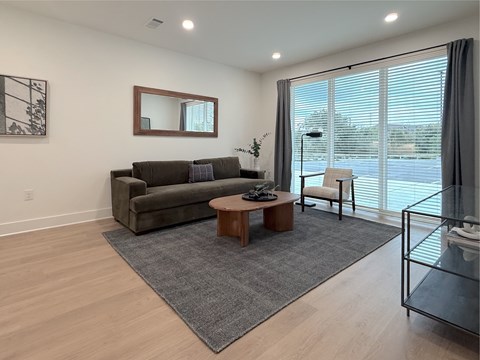 A living room with a grey rug, a brown coffee table, a grey sofa, a mirror, and a glass table.