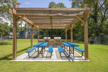A wooden pavilion with blue benches is set up in a grassy area.