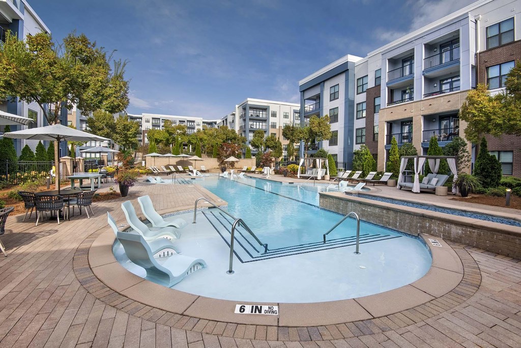 A large outdoor swimming pool surrounded by a brick patio and lounge chairs.