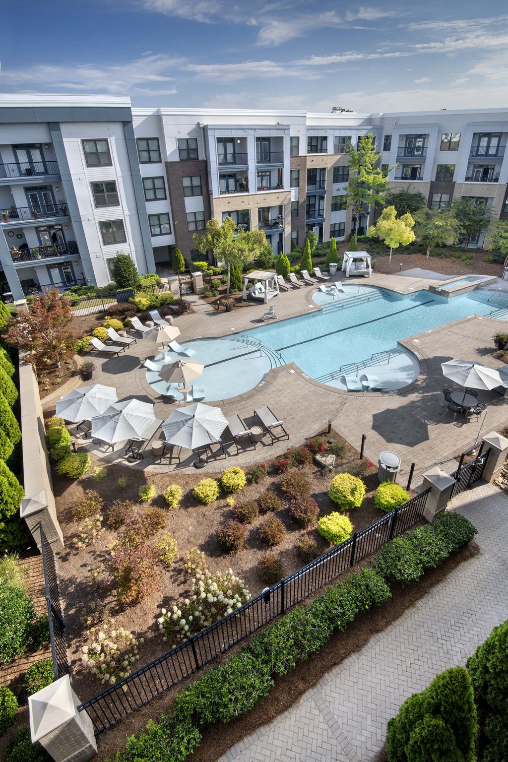 A large swimming pool surrounded by lounge chairs and umbrellas in front of apartment buildings.