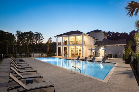 High-End Apartments in Ridgeville, SC - Preserve at Ridgeville - Resort-Style Pool with Poolside and In-Water Lounge Seats, Umbrella Tables with Chairs, and View of Clubhouse.