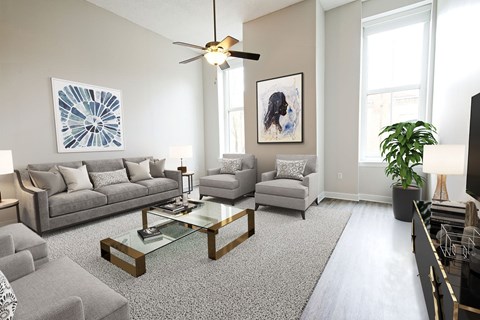 A living room with a grey couch, a glass coffee table, and a ceiling fan.