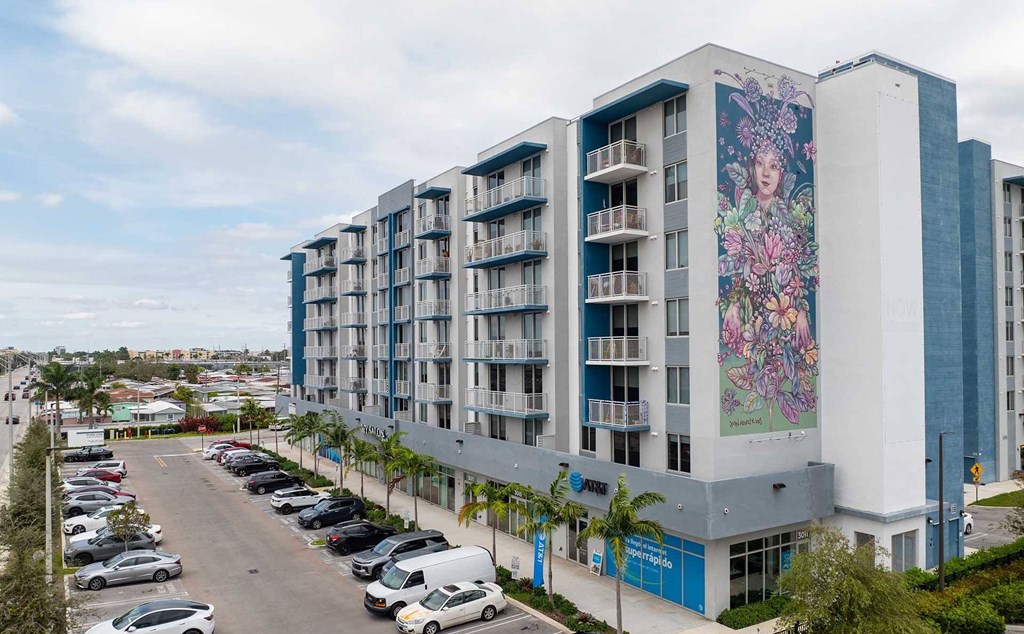 A large building with a mural on the side is surrounded by a parking lot.