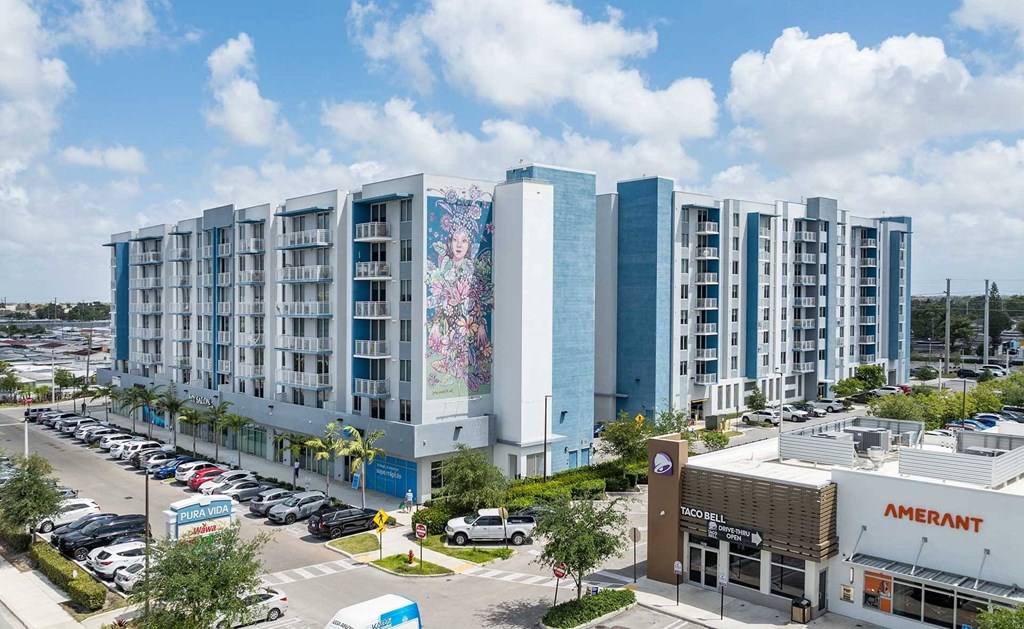 A large building with a mural on the side is surrounded by other buildings and a parking lot.