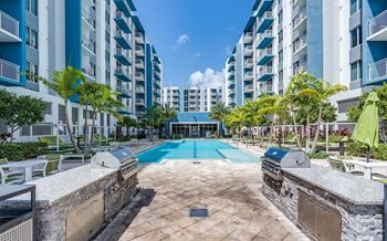A swimming pool surrounded by a stone wall and lounge chairs in front of apartment buildings.