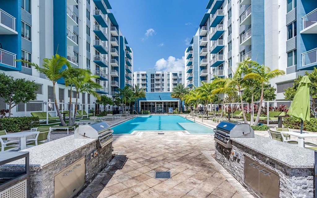 A swimming pool surrounded by a stone wall and lounge chairs in front of apartment buildings.