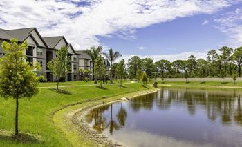 A serene landscape with a pond, a tree, and a row of houses.